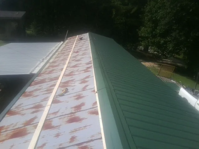 Old rusted panels beside newly installed green metal roofing — Wind Damage Roof Repair by Roofing Brothers in Libertytown