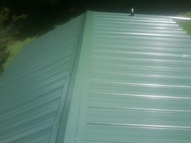 New green metal panels meeting at the ridge of a roof — Flat Roof Repair work by our crew in Libertytown