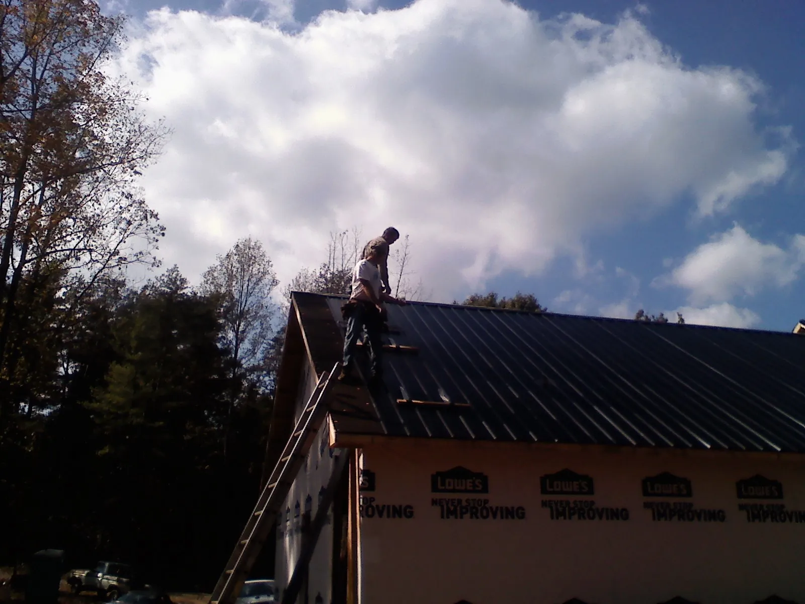 Roofer fastening dark metal panels high against a cloudy sky, from a Roof Inspection job in Libertytown
