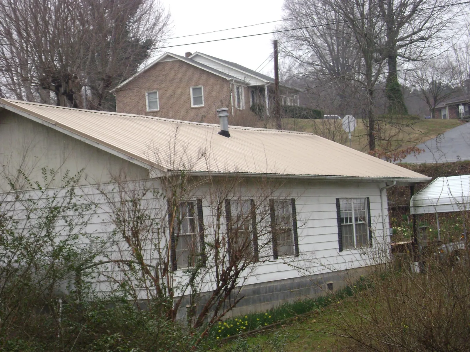 Tan metal roof on a white sided house set into a hillside — Commercial Roofing by Roofing Brothers in Libertytown